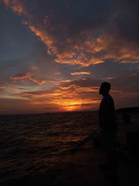 Low angle view of silhouette woman standing at beach against sky during sunset