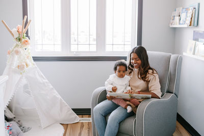 Mixed race indian mom reading book with african black baby girl toddler at home. early age education 