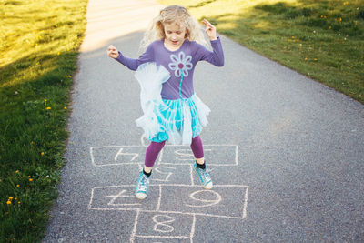 Full length of happy girl playing hopscotch on road