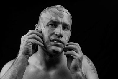 Portrait of man with adhesive bandages on face against black background