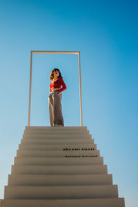 Low angle view of woman standing on staircase against clear blue sky