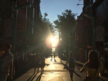People walking on sidewalk in city against bright sun