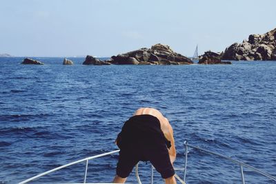 Rear view of man by railing of boat on sea against sky