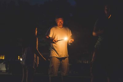 Father with daughter igniting candle while standing outdoors at night