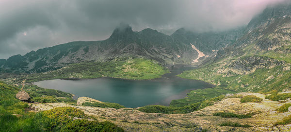 Mountain peak in fog, a lake surrounded by green grass and rocks