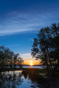 Silhouette trees by lake against sky during sunset