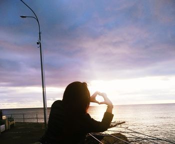 Woman sitting by sea against sky during sunset