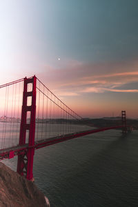 Suspension bridge over sea against sky during sunset