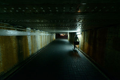 Unrecognizable person riding bike in dark underground passage with weathered walls at night in city in japan person