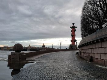 Street by footpath against sky in city