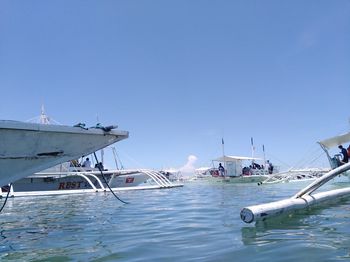 Sailboats moored in sea against clear blue sky