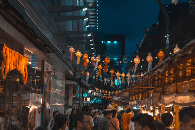 People walking on illuminated street amidst buildings at night