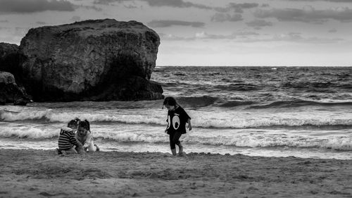 Girls playing on shore at beach against sky