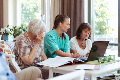 Healthcare worker and elderly women with laptop and medical reports at nursing home