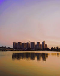 Scenic view of river by buildings against sky during sunset