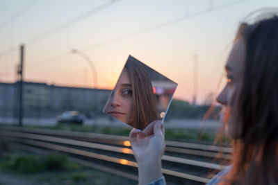 Woman holding mirror against sky during sunset