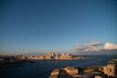 Buildings by sea against blue sky