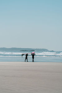 Rear view of men on beach against clear sky