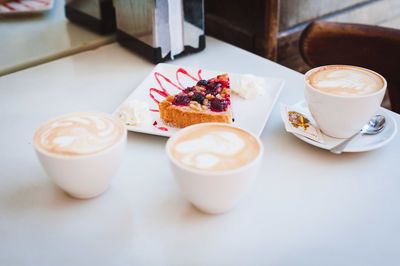 High angle view of pastry with cappuccinos served on table