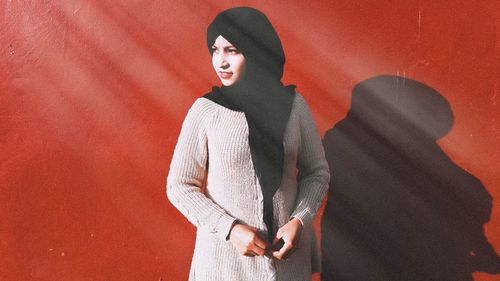 Young woman wearing hijab looking away while standing against red wall