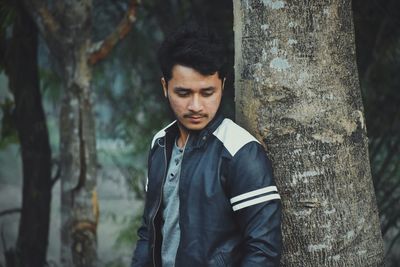 Young man standing by tree trunk in forest