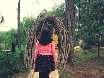 Rear view of woman standing by tree trunk in forest