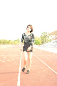 Portrait of smiling young woman running on sports track against clear sky