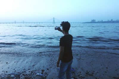 Rear view of boy standing at beach against clear sky