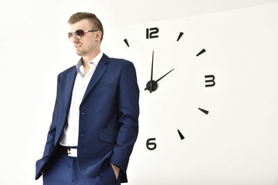 Businessman standing against clock on white wall
