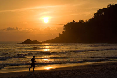 Silhouette woman on beach against sky during sunset