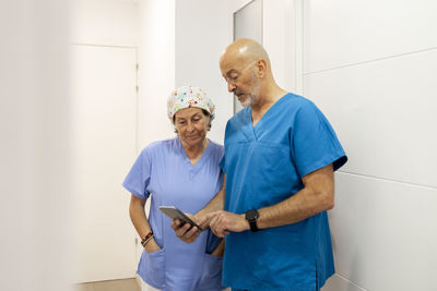 Dentist showing mobile phone to nurse standing in corridor