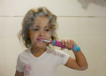 Cute girl brushing teeth in front of mirror