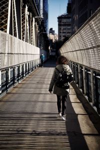 Rear view of woman walking on footbridge in city