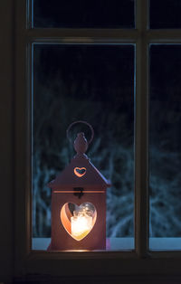 Close-up of illuminated lamp against window at night