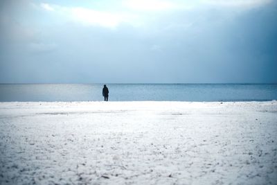 Person standing on snow covered beach against cloudy sky