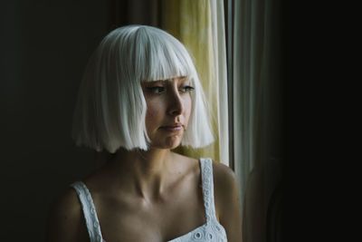 Woman looking through window while standing at home