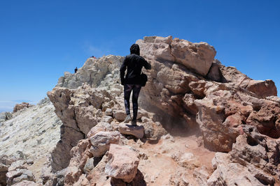 Rear view of man standing on rock against clear sky