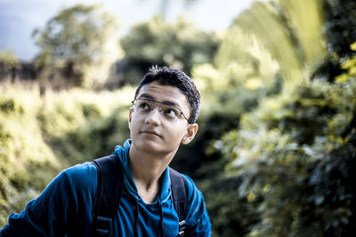 Thoughtful teenage boy standing against trees