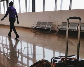 Rear view of man walking with reflection on tiled floor at airport