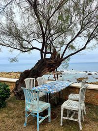 Empty chairs and table by sea against sky