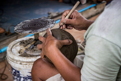 Midsection of man carving pot