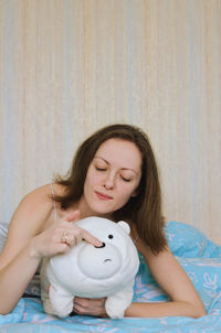 Smiling woman holding stuffed toy sitting on bed