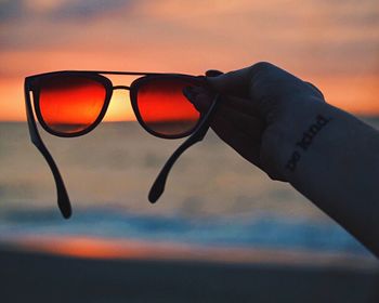 Close-up hand holding of sunglasses at beach during sunset