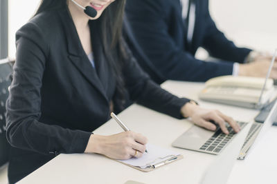 Midsection of woman using mobile phone while sitting on table