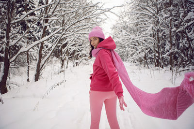 Woman run on a path in the woods in pink clothes a jacket a knitted scarf and a hat forest in winter