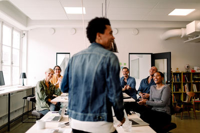 Rear view of smiling colleagues looking at businessman in office