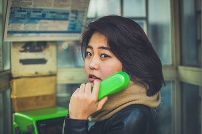 Portrait of young woman talking over telephone in booth