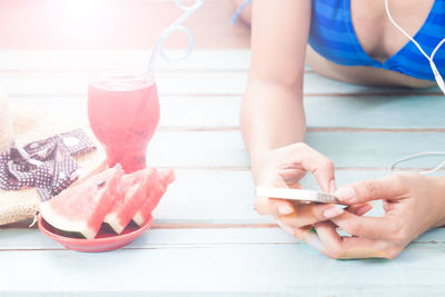 Midsection of woman in bikini relaxing by food and drink on wooden floor