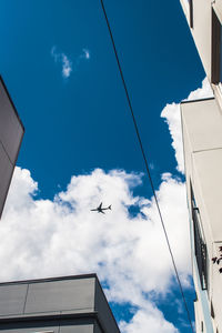 Low angle view of airplane flying over buildings against sky