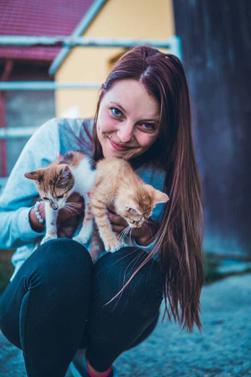 mammal, domestic animals, domestic, looking at camera, pets, portrait, smiling, one animal, vertebrate, one person, real people, young adult, leisure activity, happiness, women, lifestyles, emotion, young women, domestic cat, hairstyle, positive emotion, pet owner